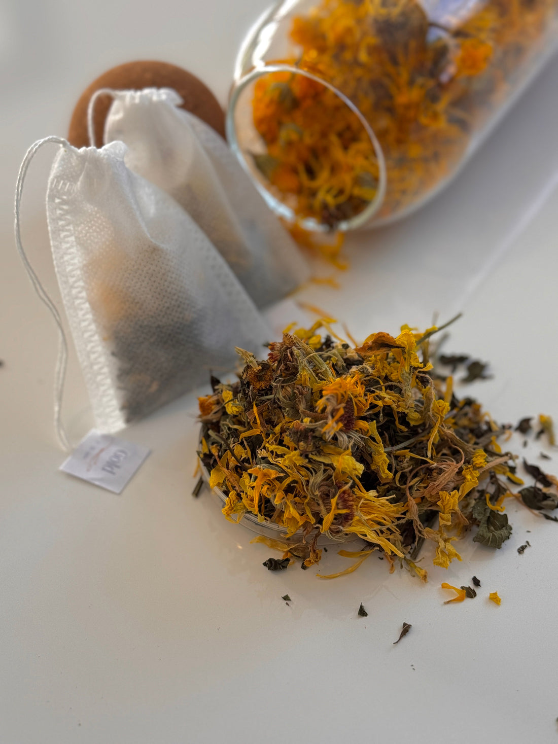 Glasdose mit losem Merifemme-Kräutertee, ganze Blätter und Blüten erkennbar
